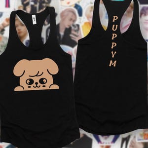 May include: Black racerback vest featuring a tan cartoon puppy graphic. The word "PUPPYM" is printed vertically on the back in tan. The vest is made of a soft material.