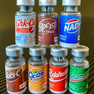 May include: Seven small glass vials with silver caps, each featuring a unique coloured label with text including Ghk-Cu, Bpc157+TB500, NAD+, Mots-C, Cjc-1295+ipamorelin, Retatrutide, and Tesamorelin. Each label also displays the text RESEARCH ONLY.