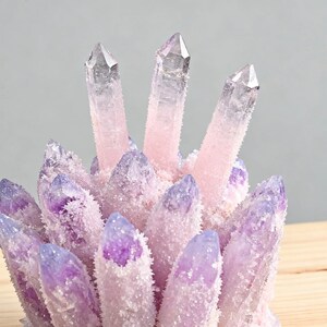 May include: A cluster of amethyst crystals with a gradient of colors. The crystals transition from a deep purple at the base to a soft pink and clear at the tips. The surface has a frosted appearance.