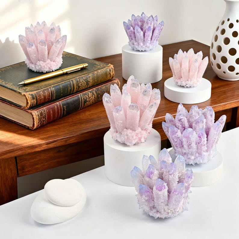 May include: Several decorative crystal clusters in shades of pink, purple, and white are displayed on white pedestals and a wooden surface. A gold pen rests on a stack of antique books. The crystals vary in size and shape, showcasing a natural, organic aesthetic.