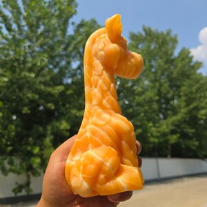 May include: A carved orange and white stone figurine shaped like a giraffe. The sculpture features a smooth, polished surface with natural swirling patterns in shades of bright orange and cream, depicting the animal in a seated position.