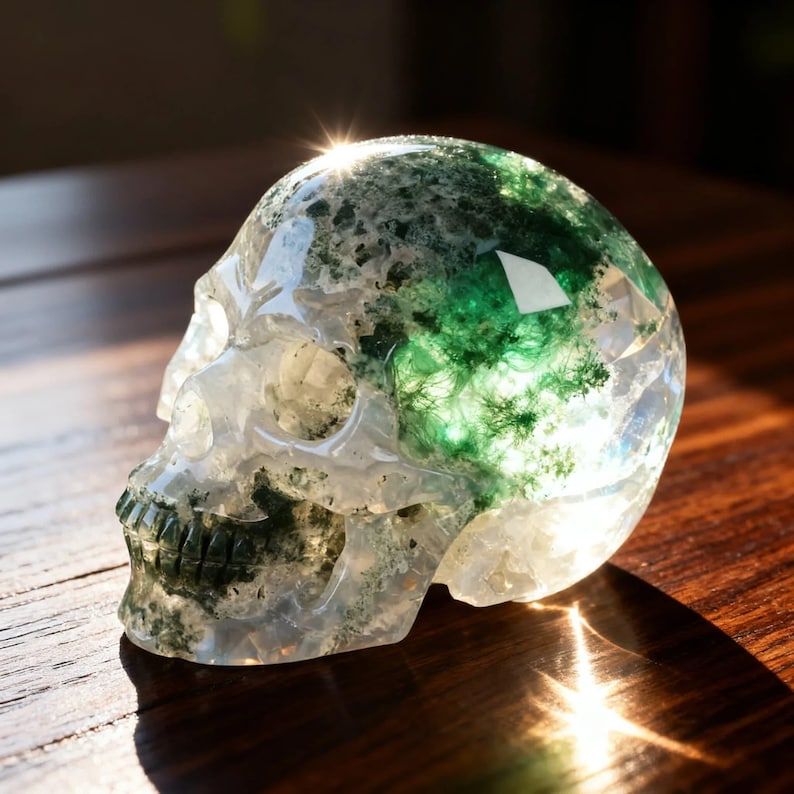 May include: A clear crystal skull with green moss inclusions. The skull is resting on a wooden surface and is illuminated by sunlight. The crystal skull is a decorative item.
