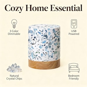 May include: A cylindrical lamp with a terrazzo pattern in shades of blue and white, atop a wooden base. The lamp is USB powered and bedroom friendly, with 3 color dimmable settings. The text "Cozy Home Essential" is at the top.