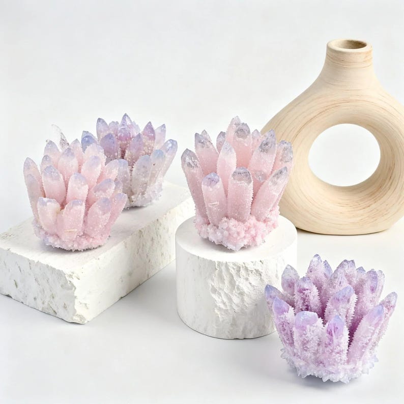 May include: Four clusters of amethyst crystals in shades of pink and purple. The crystals are arranged on white pedestals and a textured block. A beige, circular vase with a hole in the center is in the background.