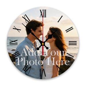 May include: A round wall clock featuring a custom photo of a couple standing by the ocean at sunset. The clock face displays black Roman numerals and black hour and minute hands with a red second hand. The text Add Your Photo Here is printed.