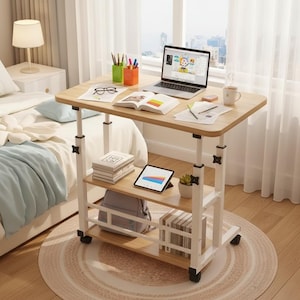 May include: A height-adjustable, rolling laptop desk with a light wood-grain top and two lower shelves. The desk has a white frame and black wheels. A laptop, books, and office supplies are on the desk. A bed and window are in the background.