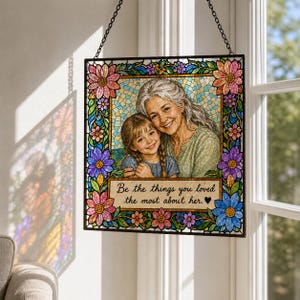 May include: A square stained glass suncatcher featuring a portrait of an older woman and a young girl. The border is decorated with colorful flowers in pink, purple, and blue. The text reads: Be the things you loved the most about her.