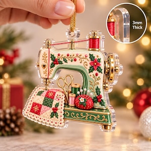 Peut inclure: Une décoration de Noël en acrylique transparent en forme de machine à coudre vintage, avec des détails verts et crème, des poinsettias rouges, du houx, un morceau de tissu matelassé, des ciseaux et des bobines. L'ornement mesure 3 mm d'épaisseur.