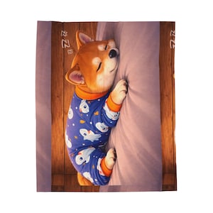 Könnte beinhalten: Ein Shiba Inu Welpe in blauem Pyjama mit weißem Fischmuster, der friedlich schläft. Der Welpe liegt an einem hellvioletten Kissen, mit einem hölzernen Hintergrund. Der Pyjama hat einen orangefarbenen Besatz.