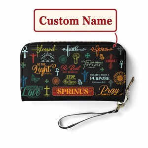 May include: A black rectangular zippered wallet featuring a colorful print of religious phrases and symbols, including crosses, sunflowers, and butterflies. The text SPRINUS is centered in a rectangular box, with a black wrist strap attached to the side.