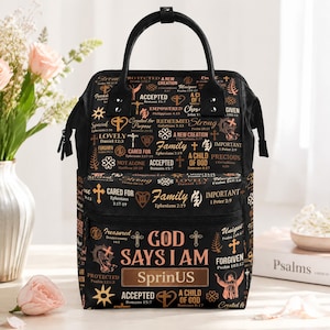 May include: A black backpack featuring a repeating pattern of gold and copper-colored religious text, crosses, and symbols. The front pocket displays the text "GOD SAYS I AM" above a rectangular box with the word "SprinUS" in bold lettering.