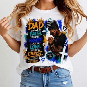 Op de afbeelding: Een wit t-shirt met een grafische print met de tekst DAD STRONG IN FAITH, BOLD IN PRAYER, RICH IN LOVE, ROOTED IN CHRIST, PROTECTOR, PROVIDER, LEADER, BUILT DIFFERENT, CHOSEN BY GOD, PSALMS 127:1 en een illustratie van een biddende man.