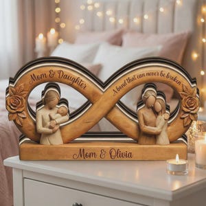 May include: Wooden infinity sign sculpture with the words "Mom & Daughter" and "A bond that can never be broken." The sculpture features carved figures of a mother and child, and a mother and daughter. The base reads "Mom & Olivia."