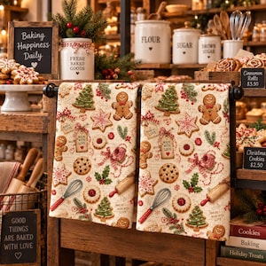 May include: Two kitchen towels featuring a repeating Christmas pattern of gingerbread people, decorated cookies, pine trees, whisks, rolling pins, and gift tags with the text Made With Love, all set against a cream background with script text.