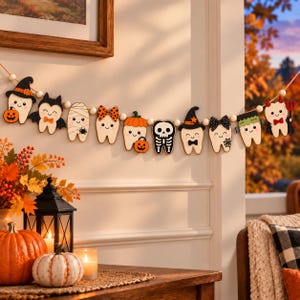 Puede incluir: Una guirnalda temática de Halloween con recortes de madera en forma de diente decorados como varios personajes, incluyendo una bruja, vampiro, momia, esqueleto y diablo, ensartados con pequeñas cuentas de madera en un cordel.