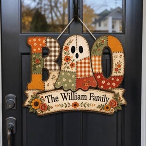 May include: A decorative wooden door sign spelling BOO with a ghost shape in the centre. The letters feature patchwork patterns of orange, green, and brown floral and gingham prints. A banner below reads The William Family with floral accents.