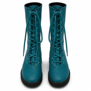 Op de afbeelding: Een paar kuithoge laarzen in de kleur blauwgroen met een vetersluiting aan de voorzijde, zilverkleurige metalen oogjes en bijpassende veters. De laarzen hebben een gladde afwerking, een ronde neus en een dikke, stevige zwarte rubberen zool.