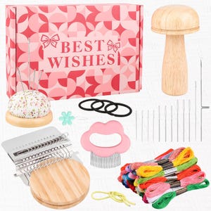 May include: A craft kit with a pink and white patterned box that reads "BEST WISHES". The kit includes a pincushion, embroidery floss, needles, a wooden mushroom-shaped tool, and other accessories for crafting.