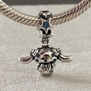 Könnte beinhalten: Ein silberner Charm-Anhänger mit einem Stern mit blauem Edelstein und einer Cartoon-Figur. Der Charm hängt an einem Silberarmband und zeigt filigrane Details.