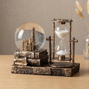 Puede incluir: Una exhibición decorativa con una bola de nieve con la Torre Eiffel, un reloj de arena de estilo vintage y una pila de libros. La base tiene un acabado envejecido y antiguo. El reloj de arena es de vidrio y metal.