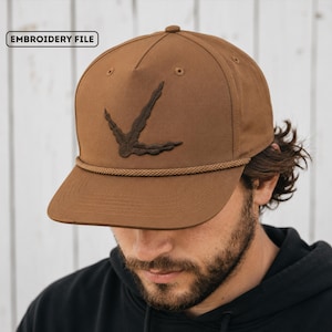 May include: A brown baseball cap featuring a dark brown embroidered bird footprint design on the front panel. The cap includes a matching brown braided rope detail across the base of the crown and the text EMBROIDERY FILE in the upper corner.