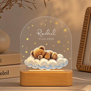 May include: An arched acrylic night light featuring a brown teddy bear sleeping on a white cloud, surrounded by yellow stars. The text "Rachel" and "11.23.2026" is printed on the acrylic. The light is mounted on a rectangular wooden base.
