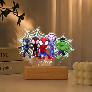 May include: An acrylic night light featuring a light blue spiderweb design with cartoon figures of Black Panther, Miles Morales, Spider-Man, Ghost-Spider, and Hulk. The name Jack is printed in white script below the figures on a wooden base.