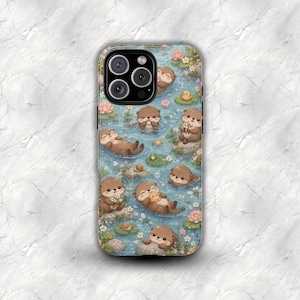 Peut inclure: Une coque de téléphone avec une illustration fantaisiste de loutres dans un étang. Le motif comprend des loutres, des nénuphars, des fleurs et un caneton, sur fond d'eau bleue. La coque a une finition brillante.