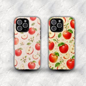 May include: Two phone cases featuring a repeating pattern of red apples, apple slices, green leaves, and white apple blossoms on a light background. The design includes small red heart outlines and star shapes scattered among the fruit illustrations.