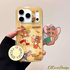 Könnte beinhalten: Gelbe Handyhülle mit Cartoon-Illustrationen von Jerry aus Tom und Jerry. Die Hülle hat einen Pop-up-Griff mit Jerry, der eine Sonnenbrille trägt und liest. Auf der Hülle stehen die Worte "LUCKY", "HA! HA" und "TOM and JERRY".