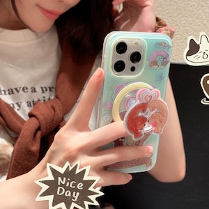 Könnte beinhalten: Hellgrüne Handyhülle mit Cartoon-Hunde-Design und Pop-up-Griff. Die Hülle hat einen transparenten Rand und den Text "donut". Ein "Nice Day"-Aufkleber ist ebenfalls sichtbar.