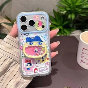 May include: Clear phone case with a blue trim, decorated with vibrant cartoon character stickers. The case showcases a playful design with various stickers, including a cartoon character with a yellow face and blue hair. The case is designed to fit a smartphone.