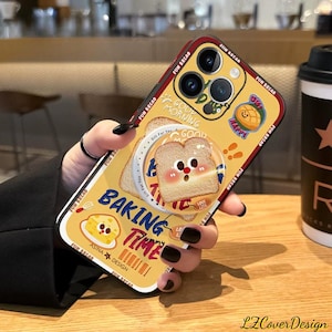May include: A yellow phone case with a cartoon bread design. The case features the words "Good Morning", "Baking Time", and "Happy". The case has a red border and a pop-up grip with a bread slice illustration.