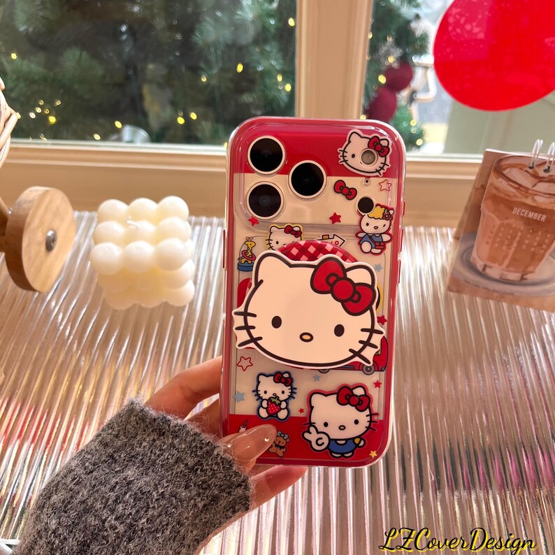 May include: A red and clear phone case featuring Hello Kitty designs. The case has a red border and a clear back, showcasing various Hello Kitty illustrations with red bows. The case is designed for a phone with multiple camera lenses.