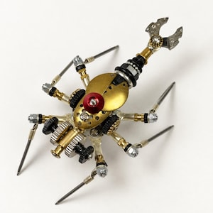 Peut inclure: Une sculpture d'insecte mécanique composée de pièces métalliques recyclées, incluant des engrenages en laiton, des tiges argentées, des anneaux en plastique noir et une pièce centrale rouge, avec une queue segmentée terminée par une pince.
