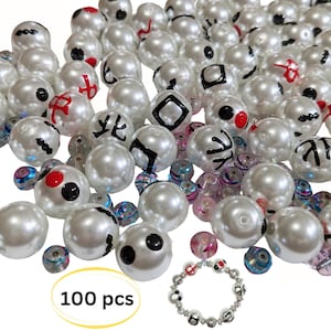 May include: A collection of 100 white pearl beads with various black and red designs. The beads are arranged in a pile, with a few scattered around. A bracelet made with the same beads is also shown in the image.  100 pcs