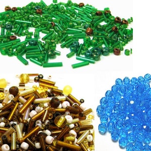 May include: Assortment of glass beads in green, gold, and blue colors. The beads are various shapes and sizes, including round, cylindrical, and faceted.