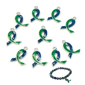 May include: Ten silver charm pendants shaped like green and blue awareness ribbons. The charms are arranged in a circle around a blue gemstone bracelet with a smaller green and blue ribbon charm.