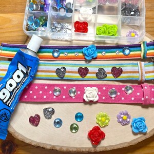 Puede incluir: Tres cinturones de cinta de colores con diferentes adornos, incluyendo corazones, flores y pedrer&iacute;a. Tambi&eacute;n se puede ver un tubo de pegamento en la imagen.