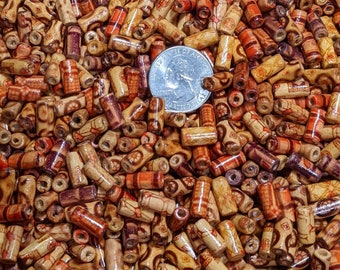 May include: A close-up shot of a pile of wooden beads with various designs and colors. The beads are cylindrical and feature patterns in shades of brown, red, and orange. A quarter is included for size reference. These beads are suitable for jewelry making and crafts.