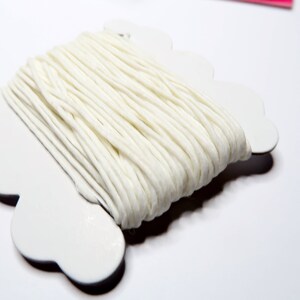 May include: A spool of white cotton yarn is displayed on a white, scalloped-edge holder. The yarn is tightly wound, showing a textured surface. This craft supply is ideal for knitting, crocheting, and other textile projects.