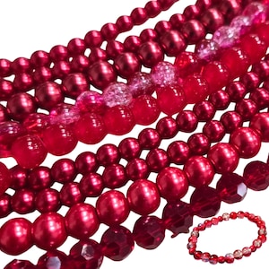 Puede incluir: Una colección de cuentas rojas con varios acabados, incluyendo texturas metálicas lisas, translúcidas y agrietadas, dispuestas en múltiples hilos. Una pulsera circular hecha con estas mismas cuentas rojas se encuentra en la esquina inferior derecha.