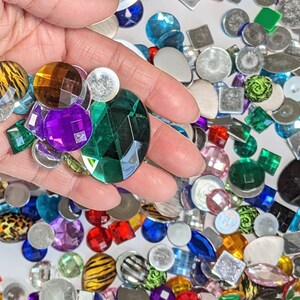 Puede incluir: Surtido de adornos de vidrio y metal de colores, incluyendo formas redondas, cuadradas y de estrella. Los adornos son de varios colores, incluyendo verde, azul, rojo, morado y dorado.