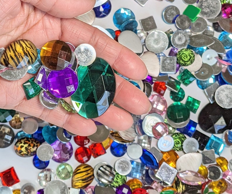 Puede incluir: Surtido de adornos de vidrio y metal de colores, incluyendo formas redondas, cuadradas y de estrella. Los adornos son de varios colores, incluyendo verde, azul, rojo, morado y dorado.