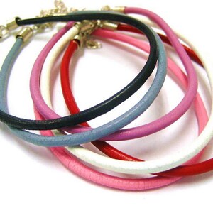 May include: A set of six leather bracelets in various colors, including black, red, white, pink, and blue. The bracelets are stacked on top of each other, showing off their different colors and textures.