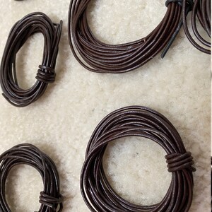 May include: Four spools of brown leather cord, each wound into a circle. The cords are different sizes, with the largest spool in the center of the image.
