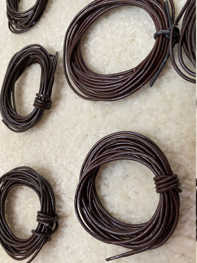 May include: Four spools of brown leather cord, each wound into a circle. The cords are different sizes, with the largest spool in the center of the image.