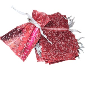 May include: A stack of red sheer gift bags with silver hearts printed on them. The bags are tied with silver ribbon and are perfect for small gifts.