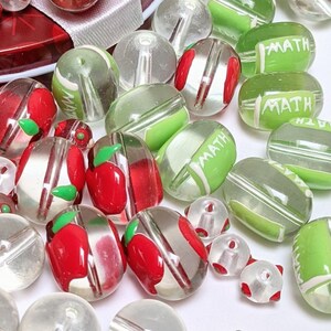 May include: Assortment of clear glass beads with red and green accents. Some beads have the word "MATH" printed on them.