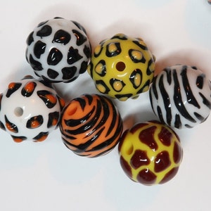 May include: Six colourful glass beads with different animal print patterns. The beads are white, black, orange, yellow, brown, and red.